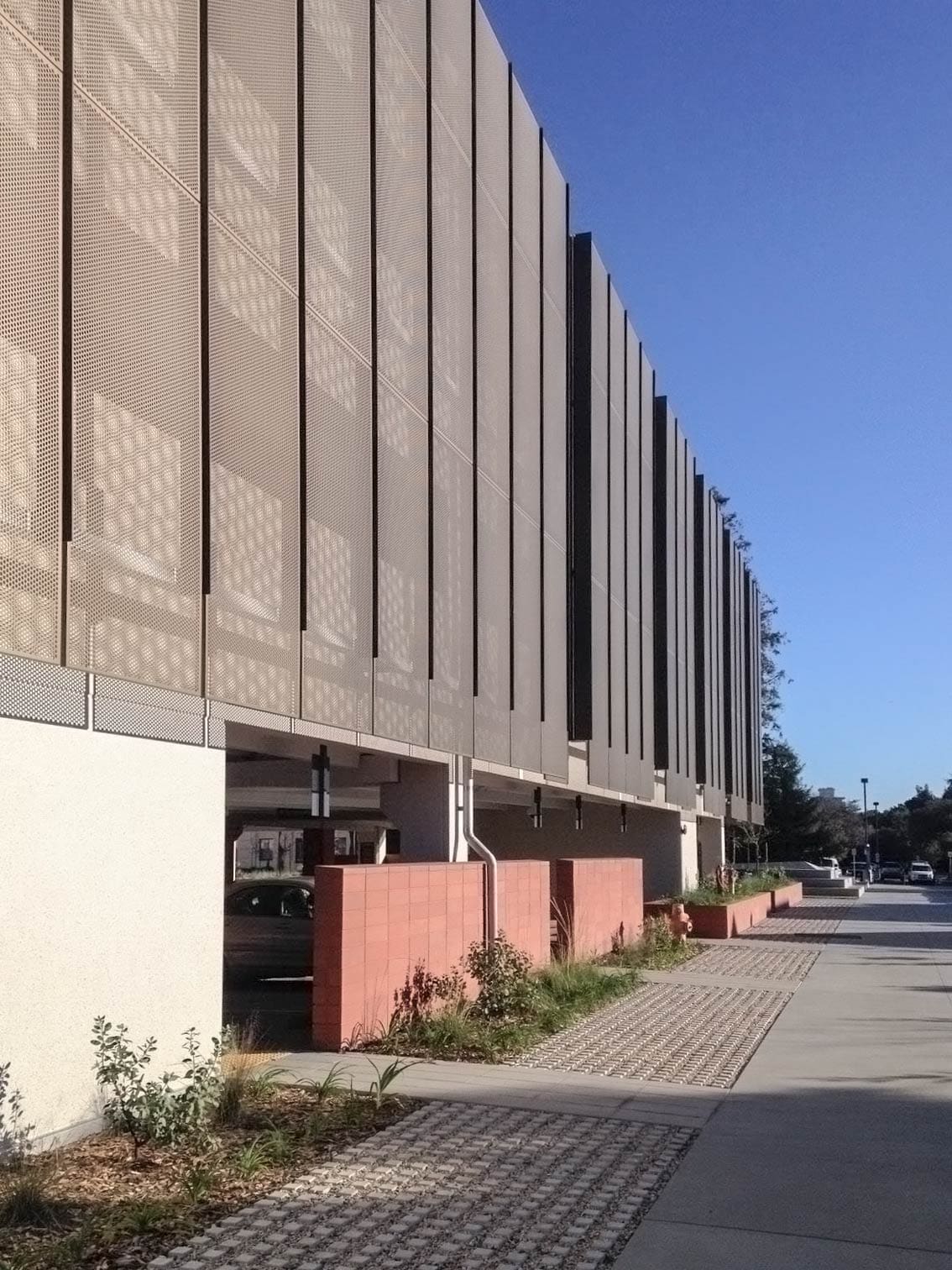 The perforated panel creates a moire effect against its shadow on the building's surface.