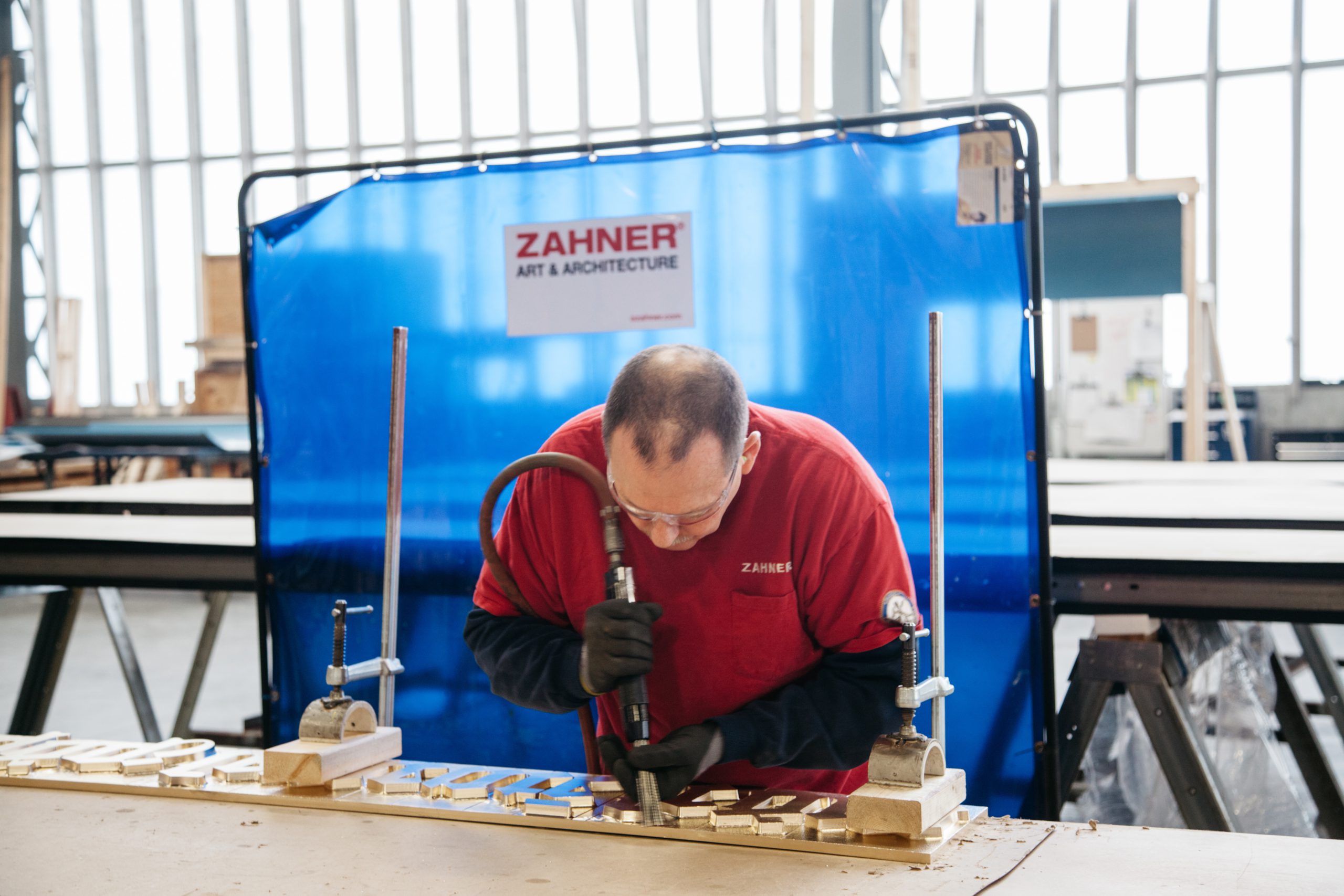 A Zahner craftsman applies a needle finish to a panel background.